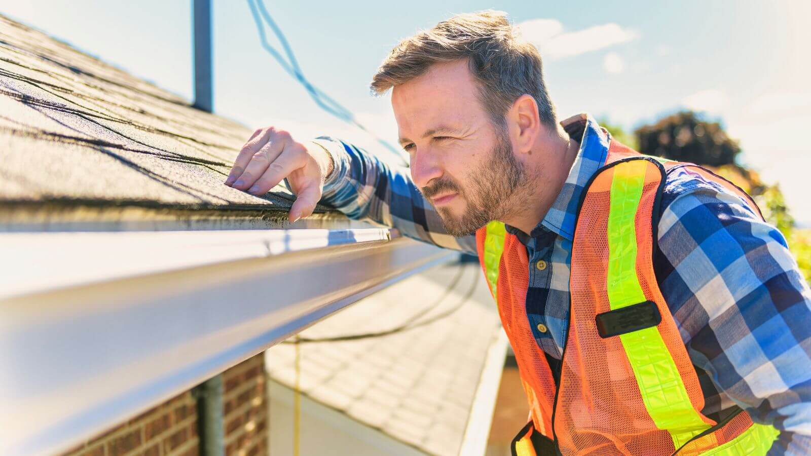 man with vest inspecting gutter