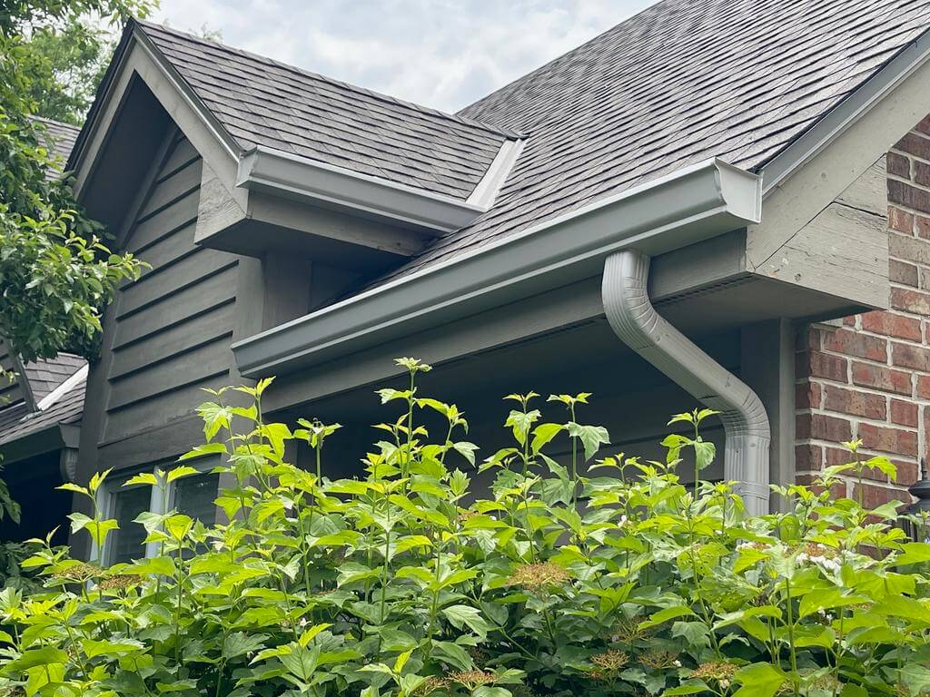 close up of a brick house with gray roof and bushes in front